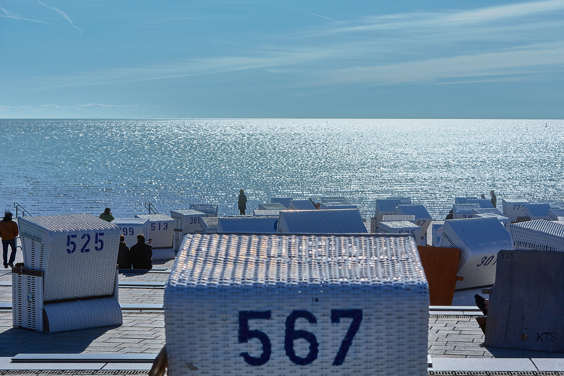 Büsum. Blick vom Deich auf die Nordsee, mit weißen Strandkörben auf der Promenade